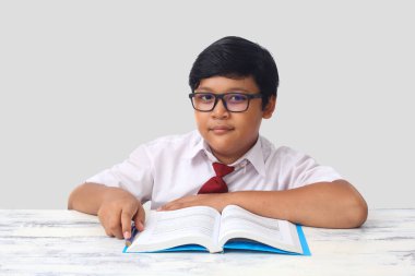 Endonezyalı bir ilkokul üniformalı Asyalı bir öğrencinin portresi çalışırken kameraya bakıyor. Gri arkaplanda izole