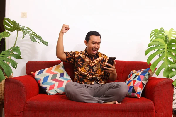 Azjaci Ubrani Typowe Indonezyjskie Ubrania Siedzą Kanapie Trzymając Smartfony Koncepcja — Zdjęcie stockowe