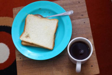 Plastik tabakta beyaz ekmek ve bir fincan kahve.