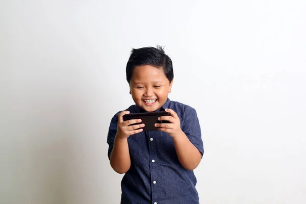 アジアの少年が立って スマートフォンでゲームをプレイ 白い壁に隔離された — ストック写真