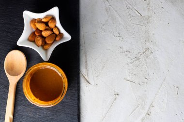 Kayısı çekirdeği yağlı cam kavanoz, tahta kaşık, fındıklı beyaz yıldız kasesi ve siyah şist plakalı kaşık ve gri çimento arka plan, kopyalama alanı. Kardiyo damar sistemi için ürün.