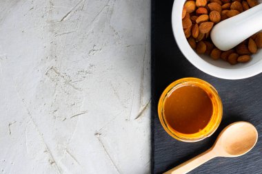 Kayısı çekirdeği yağlı cam kavanoz, ahşap kaşık, fındıklı beyaz havan topu ve siyah şist plakalı kaşık ve gri çimento arka plan, kopyalama alanı. Kardiyo damar sistemi için ürün.