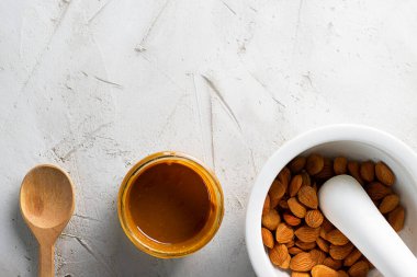 Kayısı çekirdeği yağlı cam kavanoz, ahşap kaşık, topuzlu beyaz havan topuzu ve fotokopi alanı ile desenli çimento arka planında kaşık. Kardiyo damar sistemi için ürün, vitaminler..