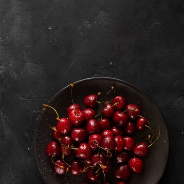Birçok olgun parlak kiraz meyvesi siyah tabakta siyah karatahta arka planda su damlalarıyla. Fotokopi alanı ile kare çekim. Tatlı, tart ve turta için taze malzeme. Organik tarım.