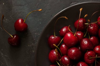 Birçok olgun parlak kiraz üzerine yakın çekim kahverengi kasede su damlaları ve yanında siyah karatahta arka planda iki dut. Yatay olarak. Tatlı, tart, turta için taze malzeme. Organik yiyecekler