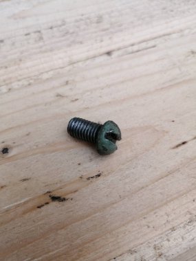 Hafif ahşap bir yüzeyde küçük yeşil bir cıvata.