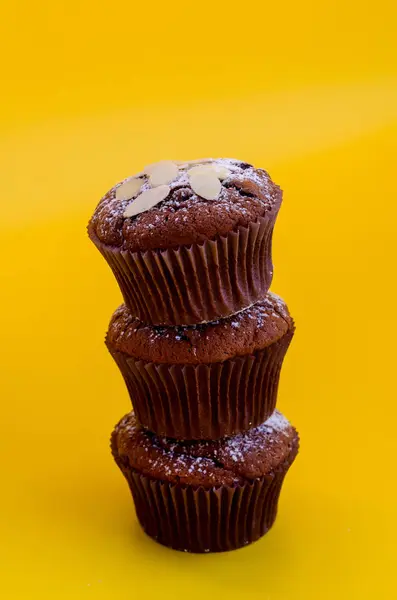 Drie heerlijke chocolade muffins op elkaar geïsoleerd op een gele achtergrond. — Stockfoto