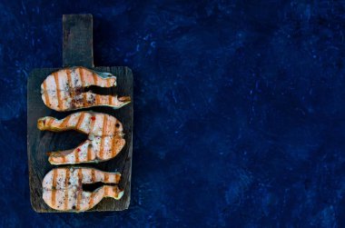 koyu arka plan alanında kesme tahtası üzerinde grup somon biftek biber tuzu üst görünümü