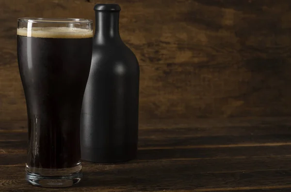 Glas en fles donker bier op houten tafel met schaduw — Stockfoto