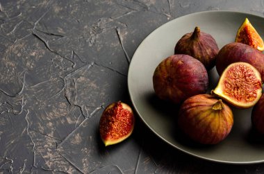 koyu gri arka plan üzerinde siyah bir tabak içinde incir