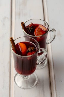 Sıcak kırmızı mulled şarap veya gluhwein cam portakal, tarçın çubukları ve beyaz ahşap arka plan üzerinde anason ile.