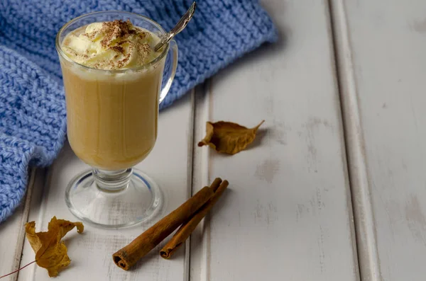 Sütőtök latte tejszínhab egy üvegedénybe egy fehér fa háttér — Stock Fotó