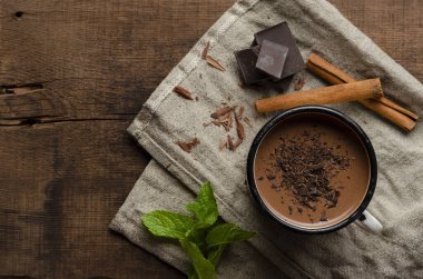 Bir fincan sıcak çikolata, tarçın çubukları, nane ve çikolata ahşap masada.