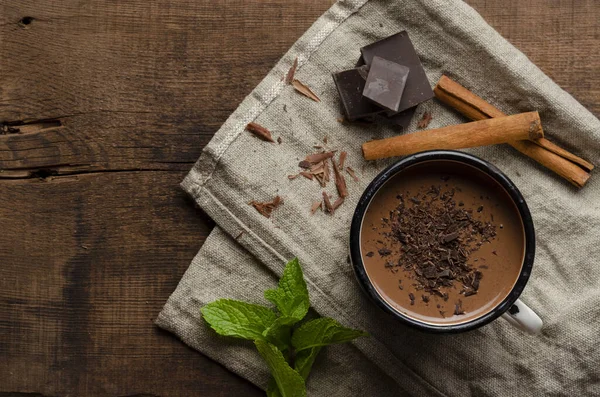 Filiżanka gorącej czekolady, paluszki cynamonowe, mięta i czekolada na drewnianym stole — Zdjęcie stockowe