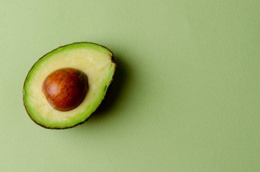Pastel yeşil arka planda yarım avokado. Basit bir arkaplanda minimalizm ve nesneler.