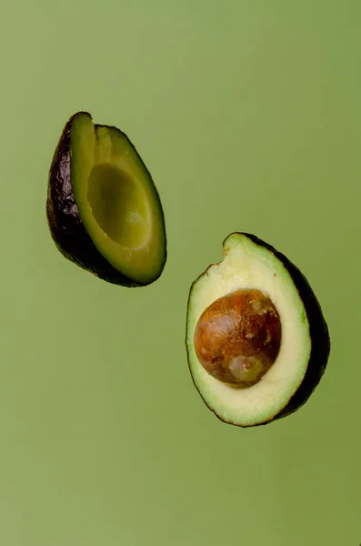 Hälften avokado flyger på pastell grön bakgrund. Minimalism och objekt på en enkel bakgrund. — Stockfoto