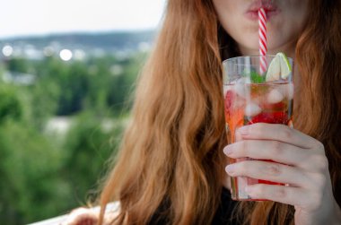 Balkondaki genç kadın soğuk taze çilek içiyor.