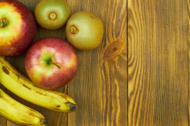 Metin için kopya alanı ile ahşap arka plan üzerinde kırmızı elma, muz ve kivi yakından görünümü. Taze meyvelerin natürmortu