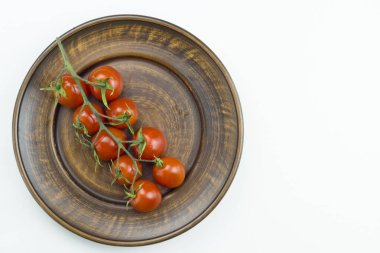 Kırmızı vişneli domateslerin üst görüntüsü beyaz arka planda izole edilmiş kahverengi tabakta su damlalarıyla dolu. Görüntüyü kapat