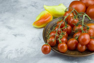 Bir tabakta taze kırmızı kiraz domatesleri ve arka planda sarı tatlı biber, metin için kopyalama alanı
