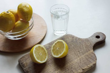 Beyaz bir masada su bardağı ile bir kapta ahşap kesme tahtası ve limon limon dilimleri