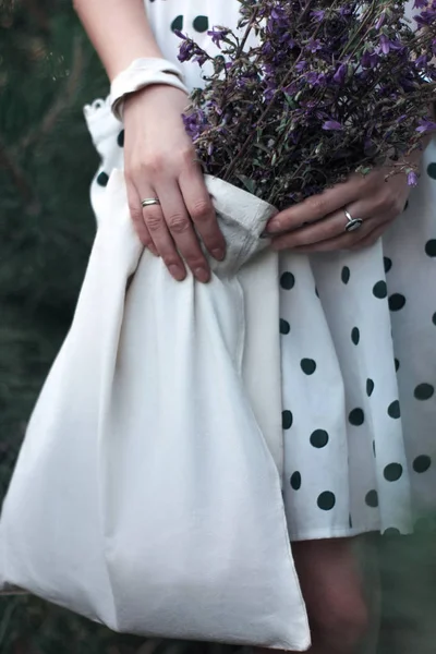 Reusable cotton Eco bag with field flowers in the hands. Young woman holding white textile grocery bag. Zero waste and conscious lifestyle