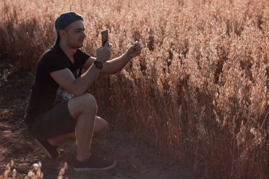 Genç adam akıllı telefonuyla fotoğraf çekiyor. Mobil fotoğrafçı görsel içerik oluşturuyor. Alanın ve doğanın fotoğrafını çekiyoruz. Açık havada, ofis dışında, doğa geçmişi olan bir adam..