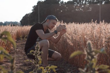 Genç adam akıllı telefonuyla fotoğraf çekiyor. Mobil fotoğrafçı görsel içerik oluşturuyor. Alanın ve doğanın fotoğrafını çekiyoruz. Açık havada, ofis dışında, doğa geçmişi olan bir adam..