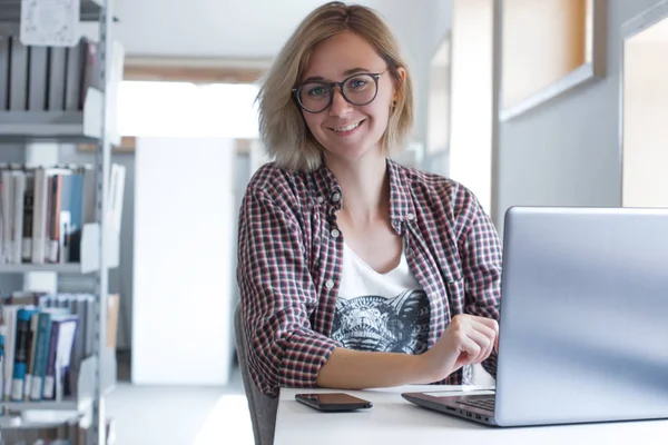 Dizüstü bilgisayarı olan bir kız. Modern ortak çalışma alanında gülümseyen serbest kız Portresi. Kütüphanede öğrenci öğrenimi. Blogger. 