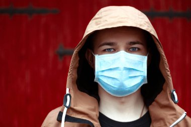 Coronavirus karantinası. Koruyucu maske takan genç Avrupalı bir adamın portresi. Salgın hastalıktan dolayı cerrahi maske takan adam, kırmızı arka plan. Tehlike durumu. Hava kirliliği 2019-NCov