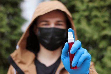 Eldivenli el dezenfektanı şişesi yakın plan. El dezenfeksiyonu iste. Coronavirus kavramını durdur. Arka planda solunum maskeli bulanık yüz. Karantina sırasında antibakteriyel jel kullanarak..