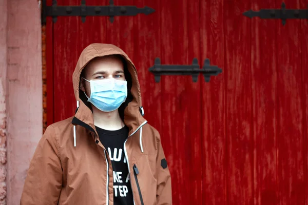 Coronavirus karantinası. Koruyucu maske takan genç Avrupalı bir adamın portresi. Salgın hastalıktan dolayı cerrahi maske takan adam, kırmızı arka plan. Tehlike durumu. Hava kirliliği 2019-NCov