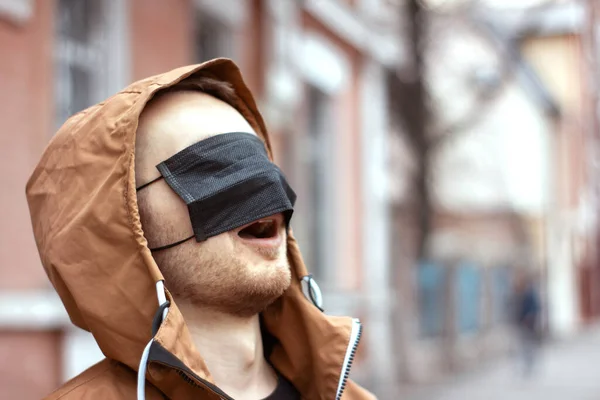 Siyah tıbbi maske takan genç adam gözlerini kapatıyor. Coronavirus karantina durumu. Gülünç bir panik maskarası. Yanlış bilgi konsepti. Virüs önleme. Salgın Covid-19.