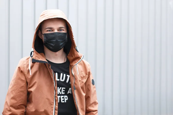 Gri arka planda siyah maskeli şık bir genç. Coronavirus karantina durumu. Salgın sırasında sokak tarzı. Tıbbi solunum cihazını pandemik giysi malzemesi olarak kullanacağız. Salgın yaşam tarzı