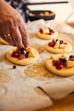 Bir kadının eli taze çöreklere meyveli çörekler koyar, fırında pişirmeye hazırdır. seçici odak.