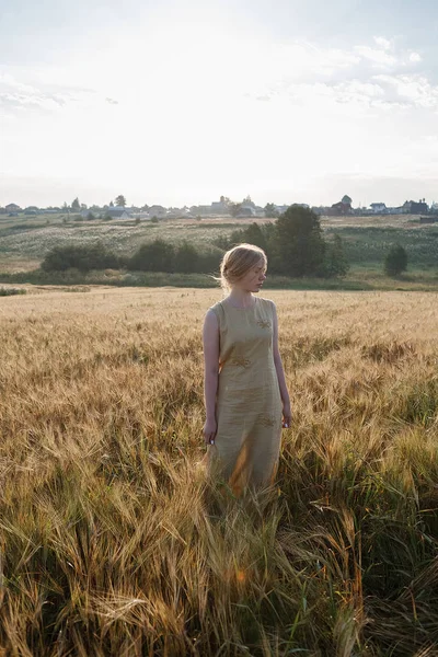 sarı elbiseli genç güzel kız yükselen güneş ışınları kulakları alanında duruyor. arka planda koru ve köy