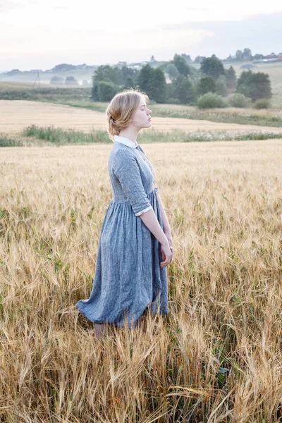 gün doğumunda kulakların altın alanda mavi eski moda açık elbise güzel sevimli genç kız. Arka planda sisli koru.