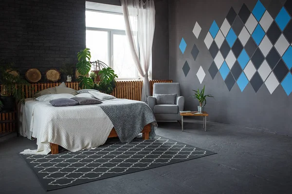 Стильный лофт уютная гостиная с двуспальной кроватью, ковер, кресло, зеленые растения и геометрические узоры на стене — стоковое фото