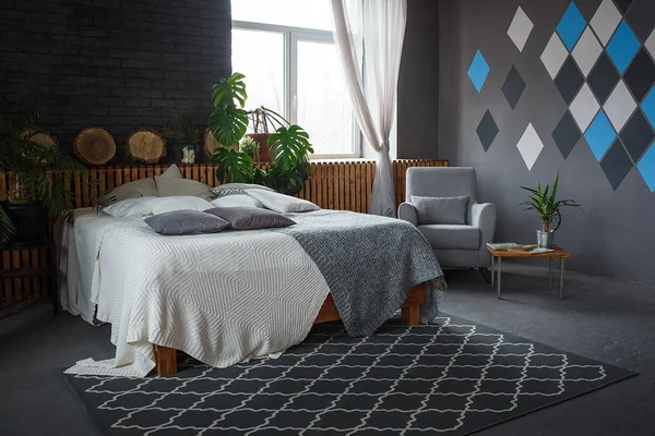 Стильный лофт уютная гостиная с двуспальной кроватью, ковер, кресло, зеленые растения и геометрические узоры на стене — стоковое фото