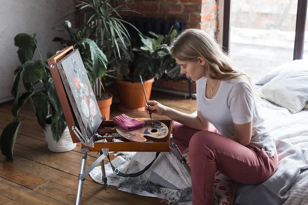 Młoda Ładna dziewczyna z pędzlem i paletą siedzi w pobliżu sztalugi rysunek obrazu. Sztuka, kreatywność, hobby, proces rysowania. — Zdjęcie stockowe