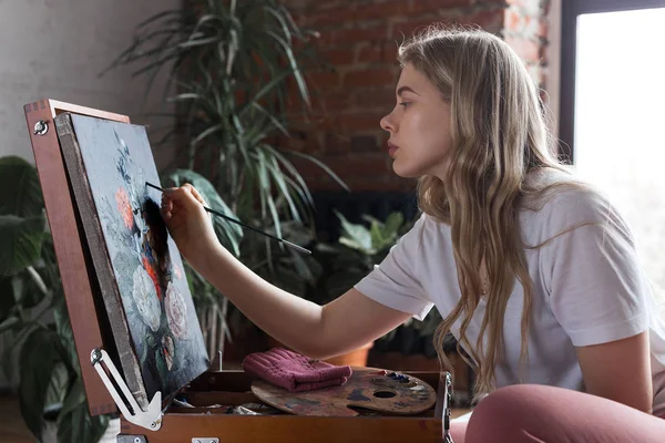 Młoda Ładna dziewczyna z pędzlem i paletą siedzi w pobliżu sztalugi rysunek obrazu. Sztuka, kreatywność, hobby, proces rysowania. — Zdjęcie stockowe
