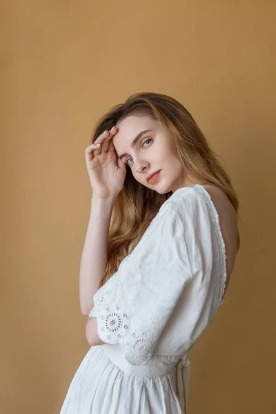 Hermosa chica flaca con el pelo largo en vestido blanco sobre fondo beige con linda sonrisa mirando a la cámara — Foto de Stock