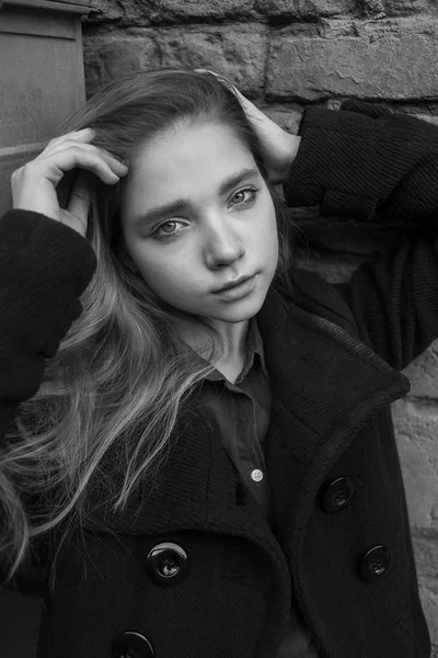 Menina sensual triste com cabelos longos em casaco preto sentado perto da parede. Conceito de melancolia. Imagem em preto e branco — Fotografia de Stock