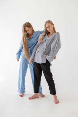 uzun sarı saçlı iki güzel genç ikiz kız kardeşler büyük boy giysiler beyaz arka plan üzerinde poz. Moda photoshoot