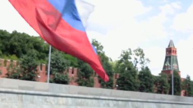 Kuleleri ve yeşil ağaçları ile kırmızı duvar fonuna karşı rüzgardan sallayarak Rus bayrağı. Güneşli bir günde Moskova'da Kremlin seti boyunca hareket