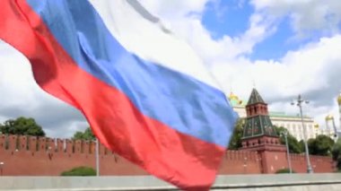 Kuleleri ve yeşil ağaçları ile kırmızı duvar fonuna karşı rüzgardan sallayarak Rus bayrağı. Güneşli bir günde Moskova'da Kremlin seti boyunca hareket