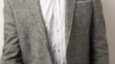 Gri ceketli, beyaz arka planda benekli gömlekli, katı beyaz bir adam yumruğunu kaldırıyor. Kameranın önünde erkek yumruğunun titremesine yakın çekim. Tehdit jesti, saldırganlık konsepti, uyarı, ceza