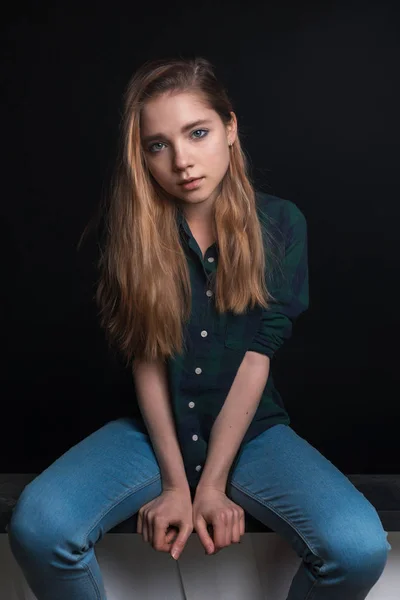 Ung sensuell flicka i rutig grön skjorta poserar på svart bakgrund medan du sitter och håller händerna framför henne — Stockfoto