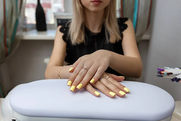 Belle fille blonde montrant des ongles de manucure jaune après la procédure dans un salon de beauté. Concept de visiter un institut de beauté — Photo