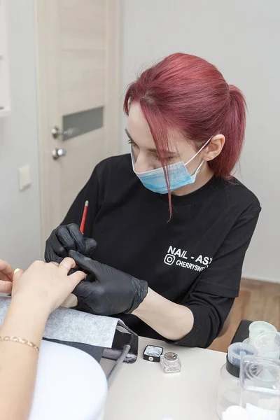 Russie, Moscou, 18 mai 2019. Maître des ongles portant un masque et des gants noirs appliquant une brosse sur les ongles en acrylique dans le salon . — Photo